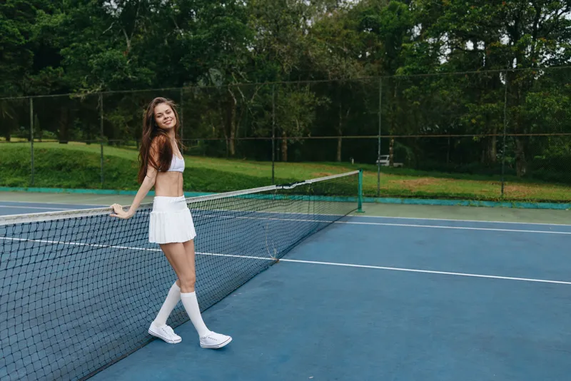 Young female tennis player smiling on a sunny court, wearing a white outfit, showcasing athleticism and joy in a vibrant outdoor setting