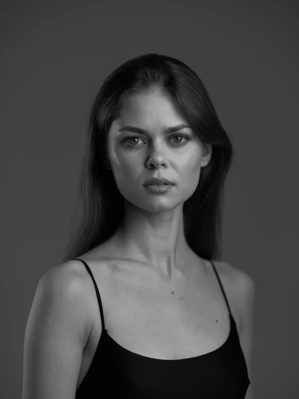 Black and white portrait of a serious woman with long hair wearing a black tank top in soft studio lighting.
