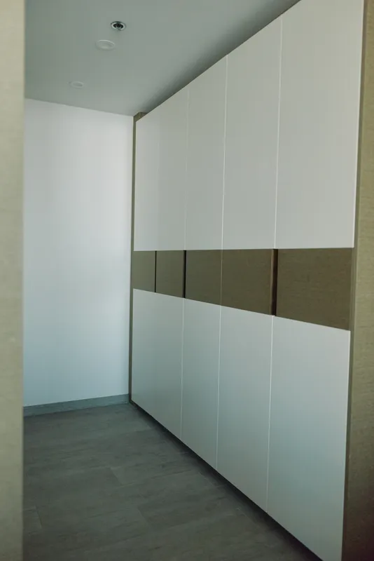 Minimalist hallway with tall white wardrobes and a brown horizontal band, clean lines, soft lighting, and a modern storage solution creating a calm, organized home interior.