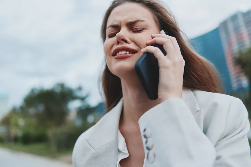 upset woman talking on phone outdoors expressing stress and frustration in casual white blazer urban background