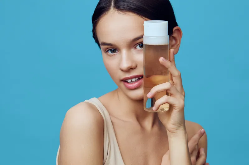 Young woman with a skincare product on a blue background, showcasing glowing skin and a fresh, natural look