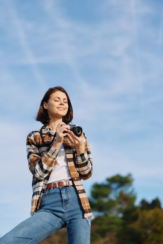 Photography, photographer, outdoor, smiling, camera in hand as a woman enjoys casual attire under a bright sky, creating candid portraits and vibrant lifestyle moments.