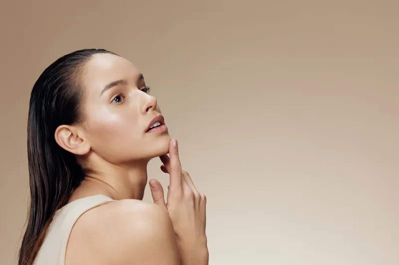 Elegant portrait of a young woman with wet hair, showcasing natural beauty and glowing skin against a soft beige background, promoting self care and skincare