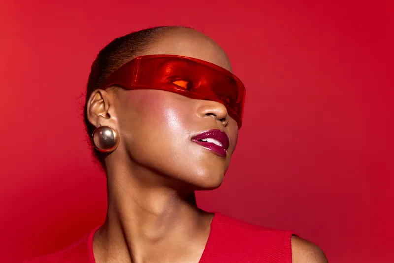 Portrait of a dark skinned African woman wearing a red blindfold and earrings, posing confidently against a red background. Concept of fashion, mystery, and empowerment.