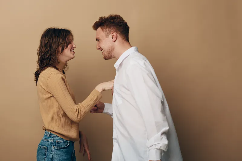Young man and woman smiling and holding hands facing each other on beige background. Concept of friendship, happiness, connection, and positive emotions between people.