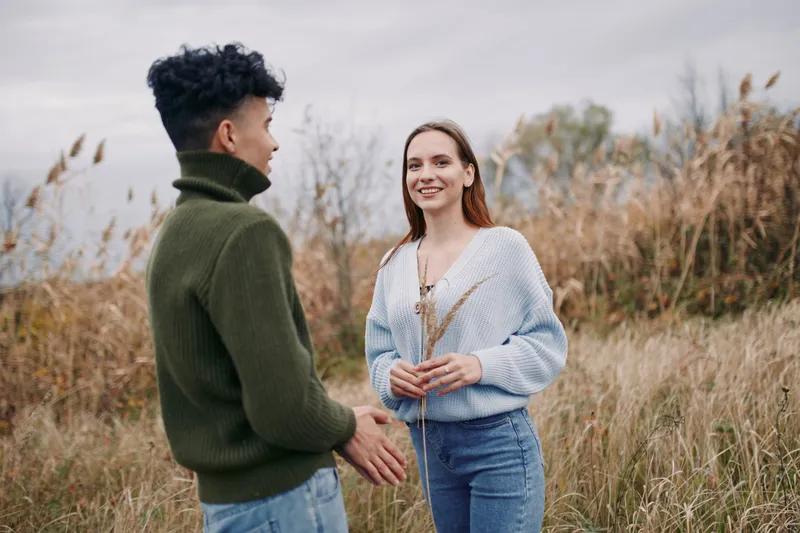 A young couple in a windswept meadow sharing a genuine conversation and relaxed body language, a candid lifestyle portrait that emphasizes authenticity and credibility in everyday connection.