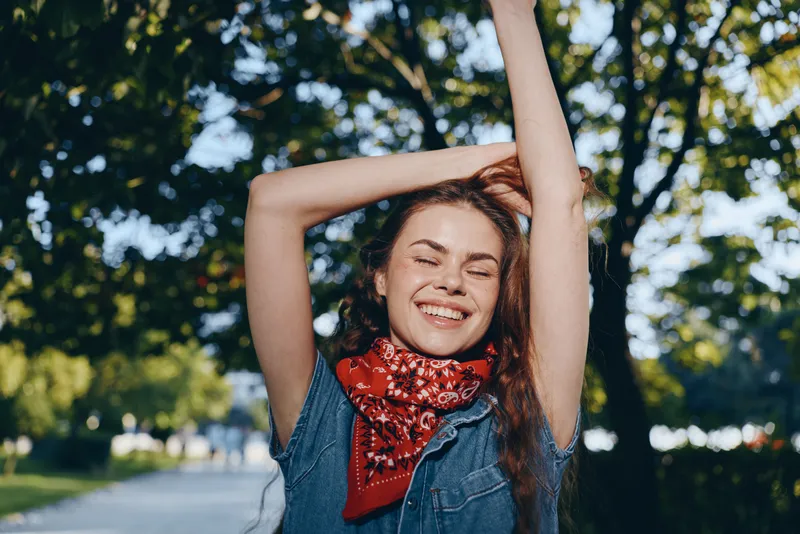 lifestyle woman in modern boho-western denim street style with red bandana smiling outdoors, film color effect, enjoying sunny day and nature background