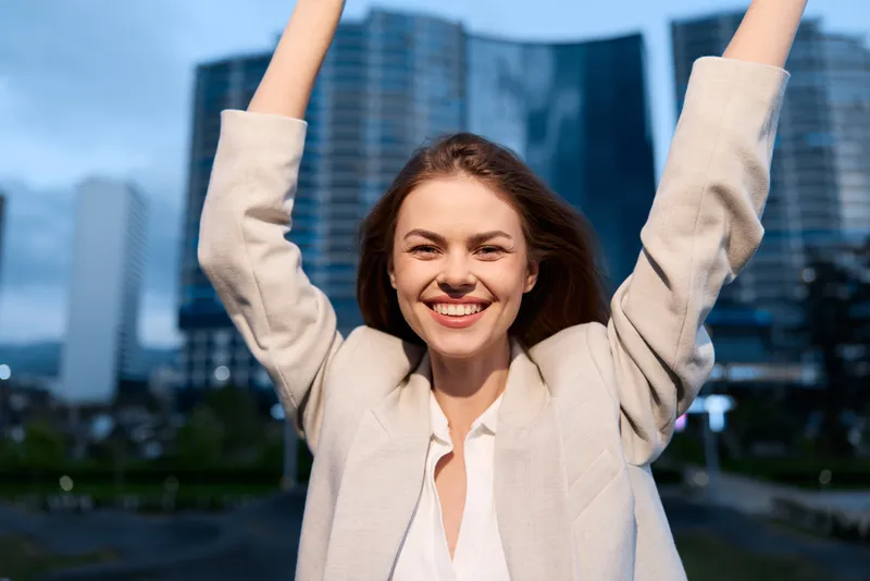Happy businesswoman celebrating success outdoors in a modern urban setting, showcasing confidence and positivity.