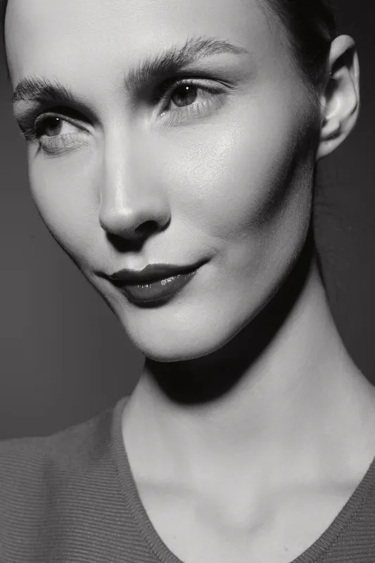 Close-up portrait of a young white woman with fair skin and short hair. She has a thoughtful expression, soft lighting highlights her facial features in black and white style.