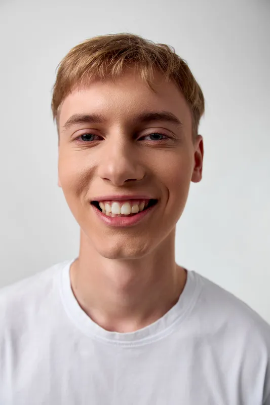 Smiling young man in a white t shirt against a plain background, capturing a friendly, approachable vibe, casual style, bright facial expression, clean studio shot without branding