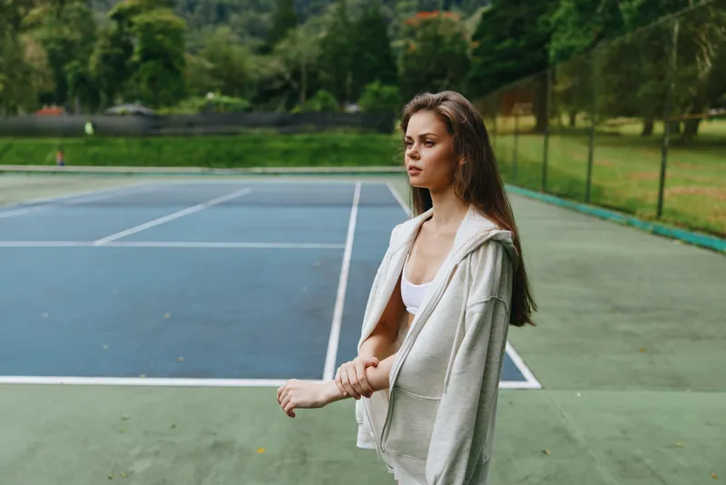 Young woman in casual athleisure wear poses on a tennis court, exuding confidence and serenity amidst a vibrant green backdrop