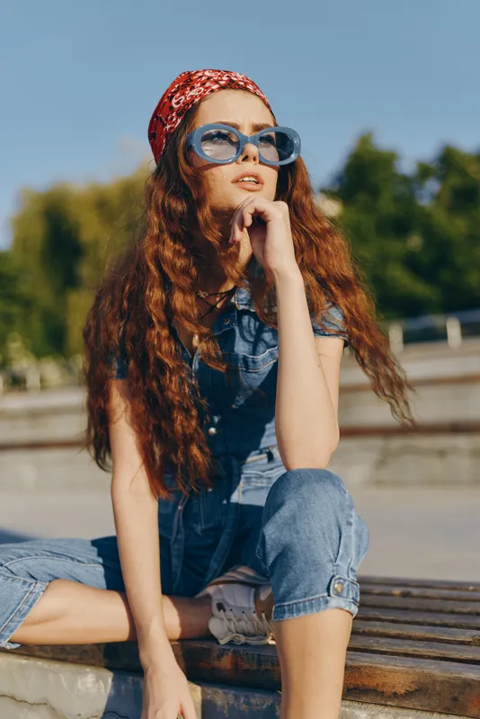 lifestyle woman in modern boho-western denim street style wearing sunglasses and red headband with long curly hair captured in warm film color tones
