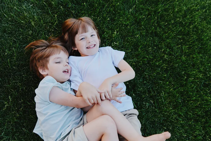 Happy children lying on green grass, enjoying a sunny day together, having fun and creating memories that last forever in a playful atmosphere.