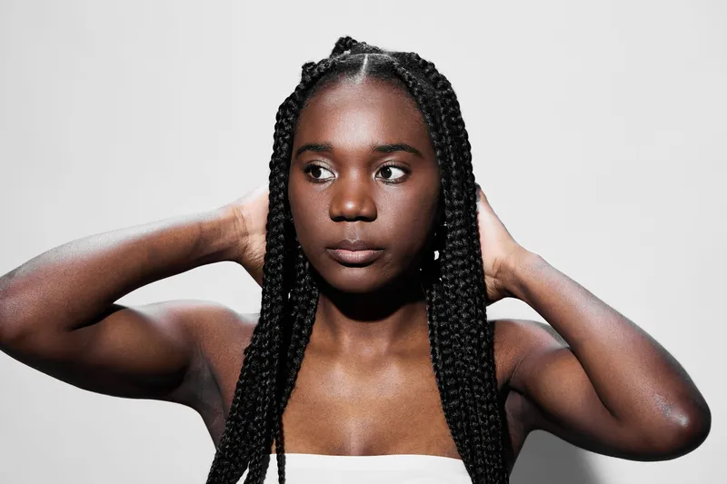 Confident young Black woman with braids posing against a minimalistic gray background, showcasing beauty and self expression during a fashion shoot