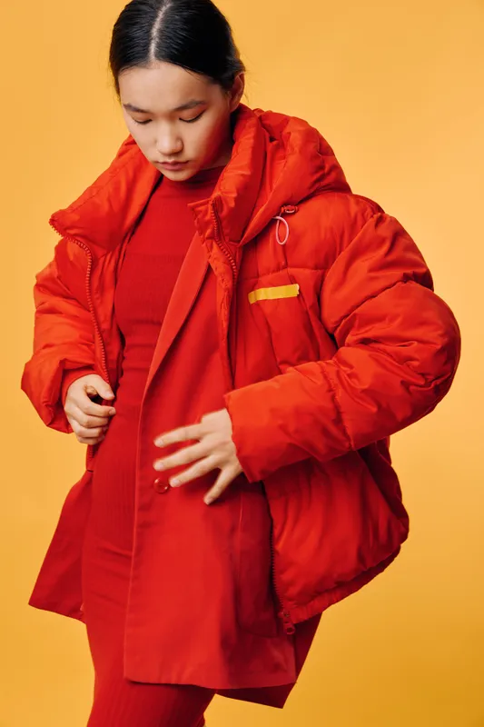 Young woman in red puffer jacket and red outfit standing against yellow background. Casual fashion, winter clothing, style, isolated, warm coat and relaxed look.