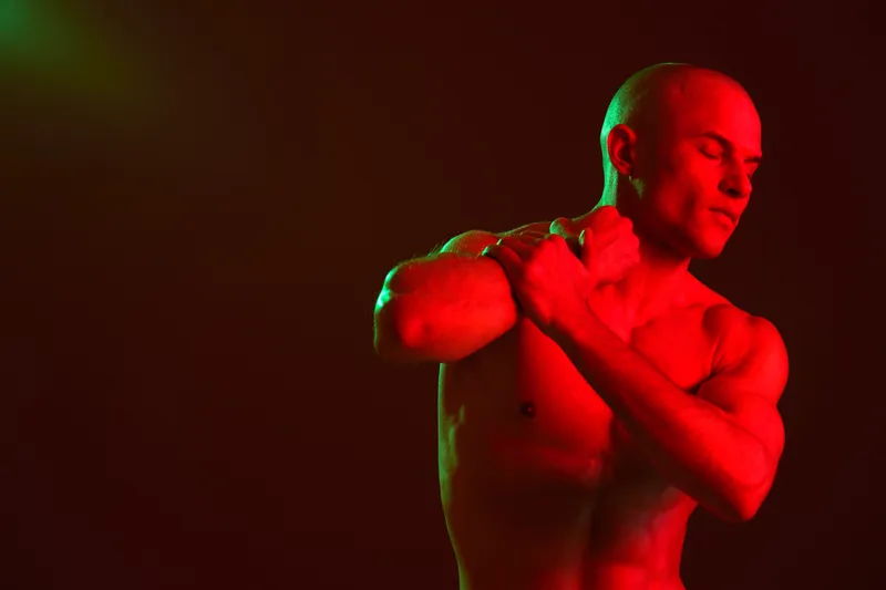 Muscular man posing with artistic lighting, creating a vibrant atmosphere. The image showcases bold colors and dramatic contrasts for a striking visual experience.
