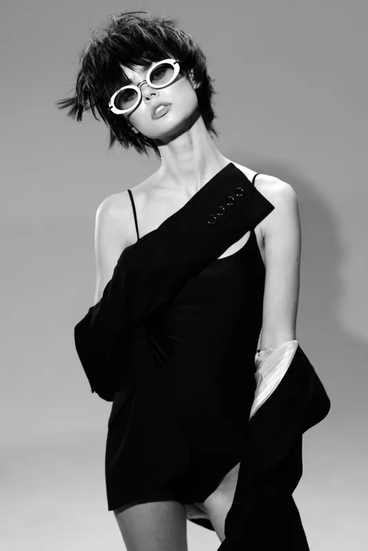 Black and white stylish woman in sunglasses posing with elegant black outfit in studio lighting.