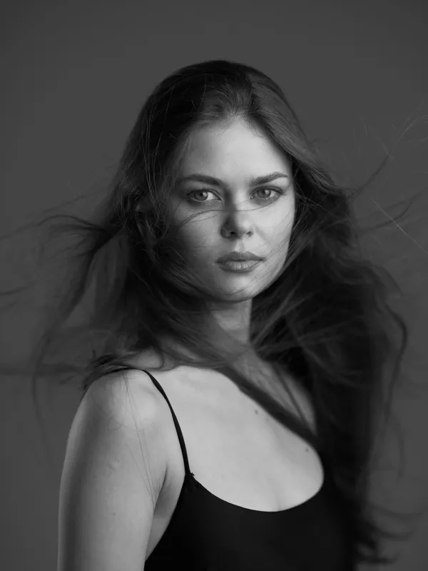 Black and white portrait of a young woman with loose hair wearing a black top, expressing calm and confidence.