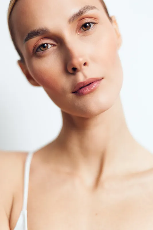 Close up portrait of a calm woman with soft lighting, clear skin, and neutral face, isolated on white background, highlighting facial features and serenity
