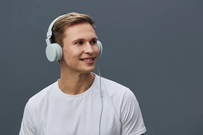 Smiling man wearing white t-shirt and large headphones looking to the side, studio portrait on plain dark background, casual person lifestyle concept, cheerful expression, auditory experience, modern 