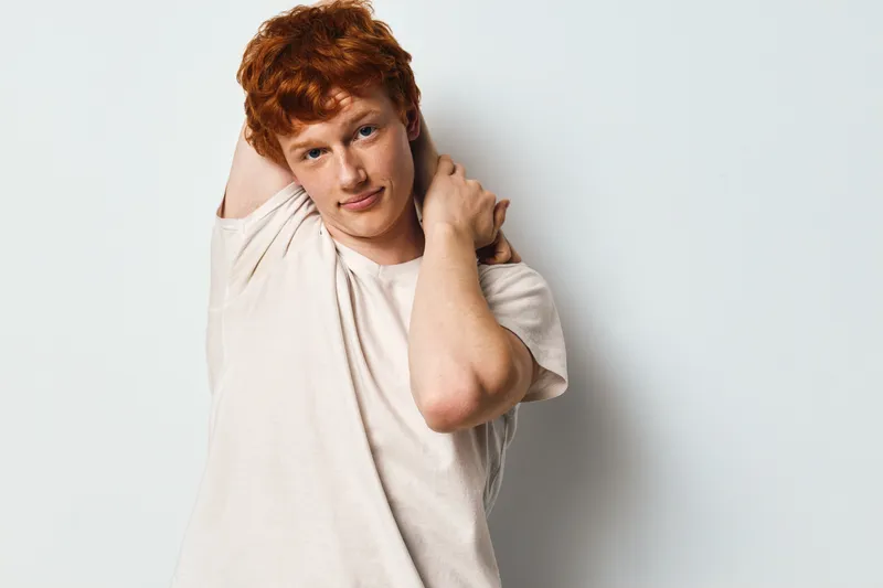 Young man with red hair and casual t shirt posing relaxed against white background, looking at camera with neutral expression and natural light in studio.