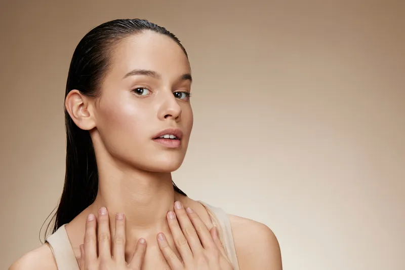 Young woman with wet hair showcasing a natural beauty look, soft lighting, neutral background, healthy skin and a confident expression reflecting the essence of skincare