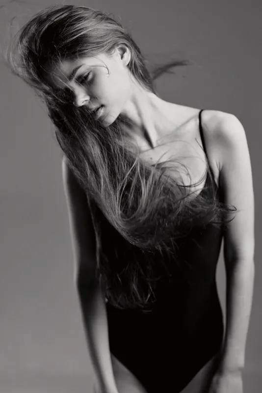 Black and white portrait of a young woman with flowing hair in a sleeveless outfit expressing calm emotion.