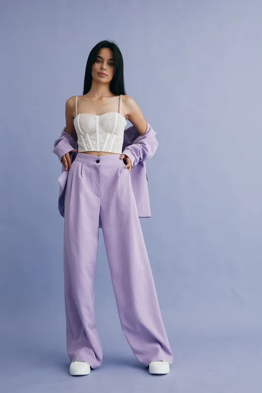 woman in lilac pants and white corset top posing in studio with light purple background, casual fashion, long black hair, confident expression, modern style