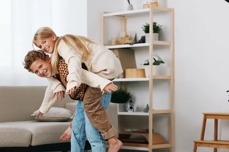 Authentic playful lifestyle moment showing a couple sharing a piggyback game at home, warm smiles and candid mood, conveying real life joy, connection, and spontaneous fun.