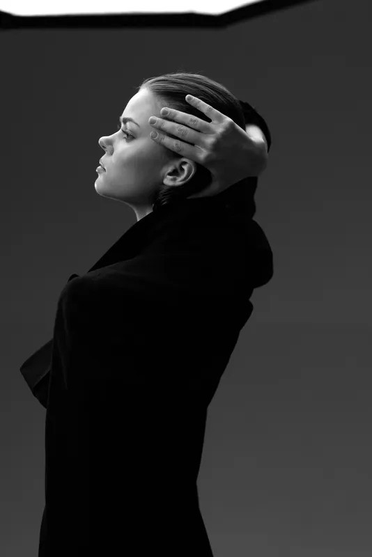 Black and white portrait of a thoughtful woman with braided hair wearing a coat, showing calm and elegant mood in minimalistic style.