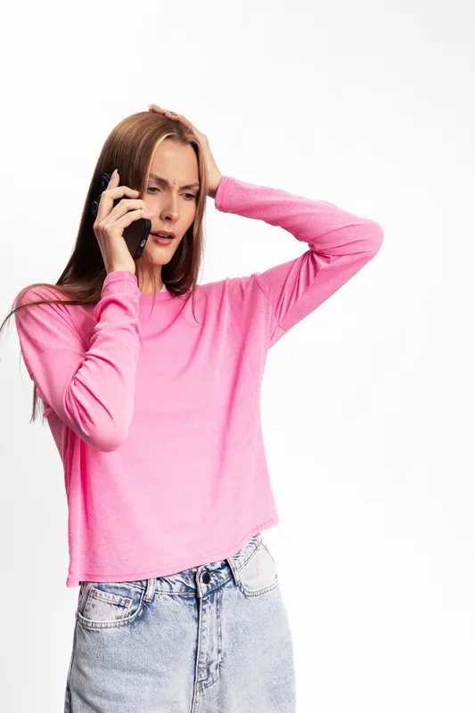 Stressed woman in pink sweater holds phone to ear and touches head, showing frustration and concern. Isolated on white background. Concept for communication problems and emotional distress.