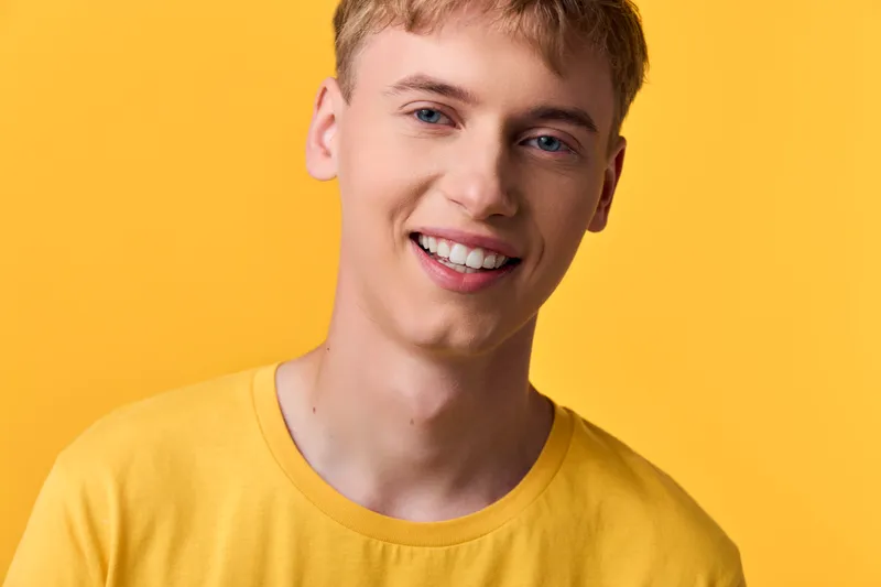 Man with a bright smile in a yellow tee against a vibrant background, a colorful friendly vibe perfect for lifestyle fashion or promotional use with a sunny warm tone