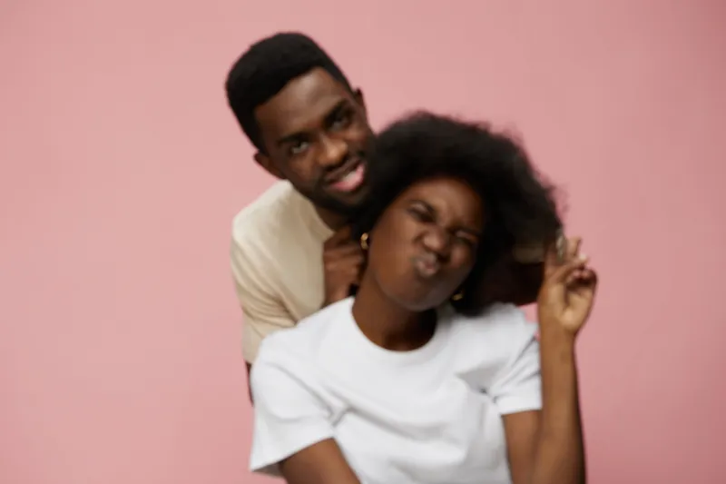Young African couple enjoying a playful moment against a soft pink background, showcasing vibrant emotions and diverse styles, perfect for joyful lifestyle themes