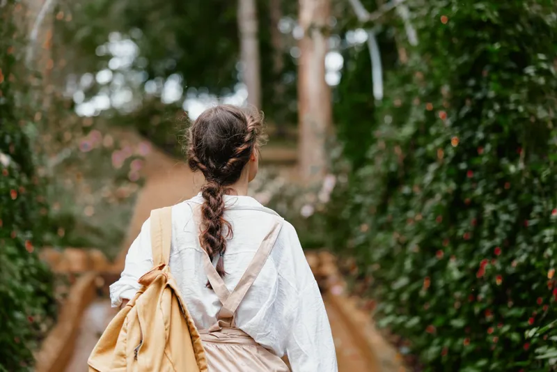 Woman walking through a lush garden wearing stylish, casual attire, exuding a sense of peace and connection with nature, ideal for promoting wellness and outdoor lifestyle