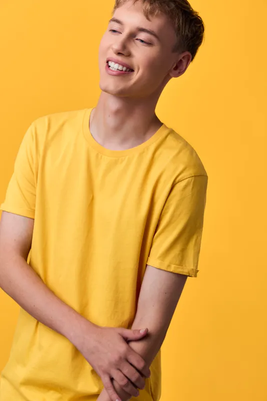 Smiling young man in a yellow t shirt stands against a bright yellow backdrop, relaxed pose, casual fashion, warm lighting and a cheerful mood for lifestyle, catalog or advertising usage