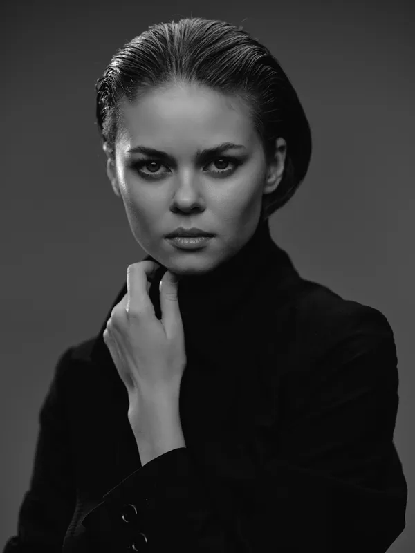 Black and white portrait of a serious woman in dark clothing with slicked-back hair and intense gaze