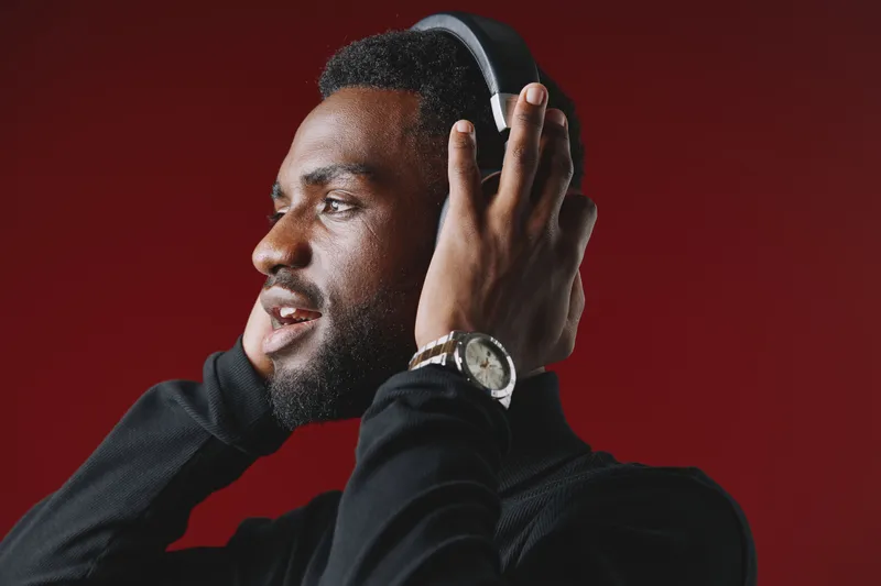 A young Black man enjoying music with headphones on a red background, portraying happiness and engagement in sound A stylish look with modern attire