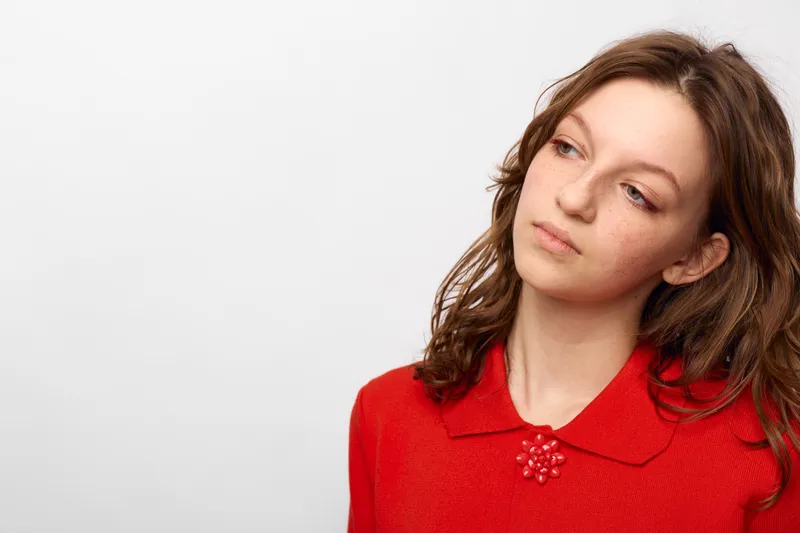 Young woman in red sweater looks away thoughtfully on white background. Concept of contemplation, emotion, and casual fashion with natural light and soft expression.