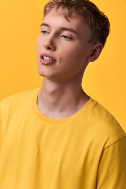 Close up of a young man with light skin wearing a yellow tee against a bright yellow backdrop, conveying casual style, confidence, and contemporary fashion for lifestyle and branding