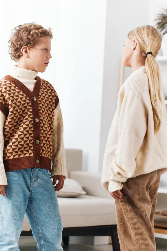 Authentic scene of two children engaging in a playful moment at home, showcasing school inspired attire, casual lifestyle, and genuine interaction in a bright living space.