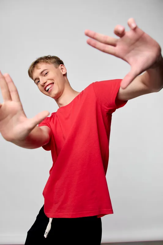 Youth energy movement playfulness action red shirt hands dynamic studio image showing a smiling male in a red tee reaching toward the camera for a playful energetic shot, capturing motion and