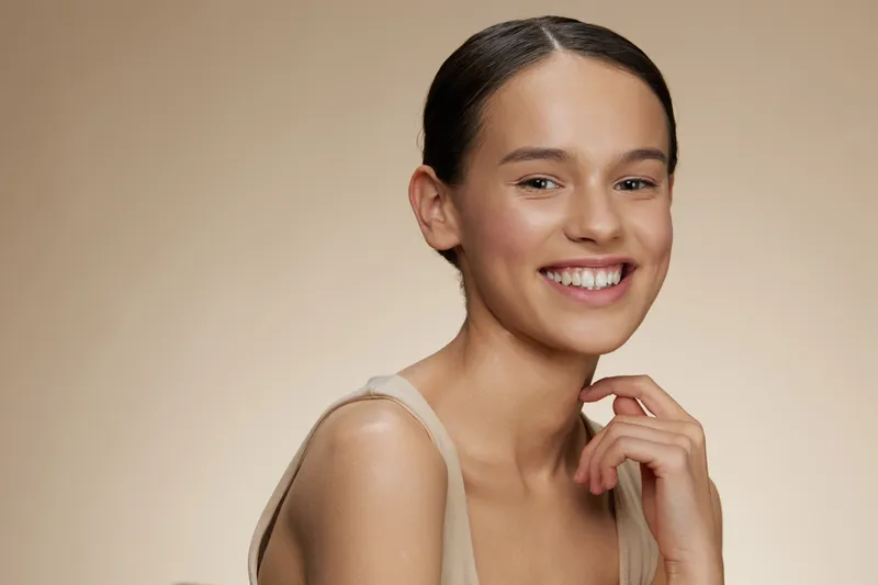 Happy young woman smiling gently in a soft, neutral background, conveying beauty and freshness with a focus on natural skincare and wellness