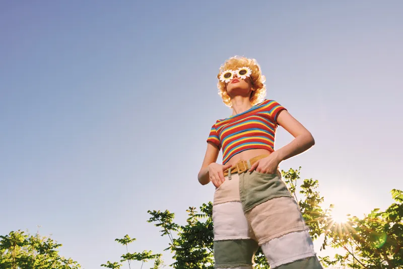 A woman in a striped top and floral sunglasses stands outdoors in bright sunlight, embracing a carefree lifestyle with a retro color palette and sunny mood.