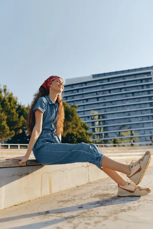lifestyle woman in modern boho-western denim street style sitting outdoors enjoying sunny day with relaxed pose and film color tones