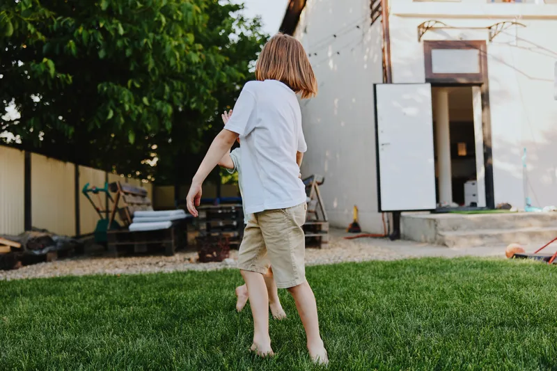 Happy child running outside in a green backyard, enjoying a sunny day with a carefree spirit and natural surroundings. Perfect for summer-themed projects.