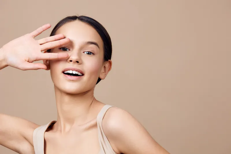 Smiling young woman with natural beauty showcasing confidence on a neutral background, perfect for healthy lifestyle and beauty themes