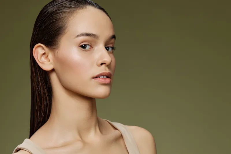 Elegant female model with long hair, showcasing natural beauty against a green background, epitomizing confidence and serenity in a fashion forward look