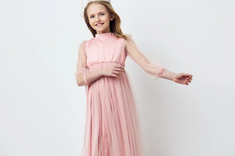 Young girl in a pink tulle dress, smiling joyfully, against a soft white background, embodying childhood innocence and happiness in a seasonal fashion concept