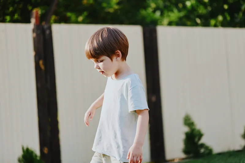 Thoughtful boy walking outside, enjoying nature and exploring the surroundings, showcasing curiosity and innocence in a serene backyard setting.