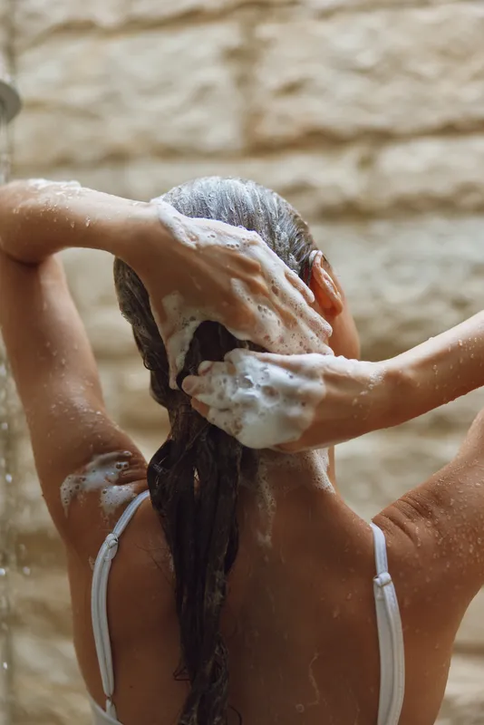 Woman washing hair with shampoo foam in shower, wet skin, natural light, spa-like atmosphere, clean and refreshing morning routine, wellness concept.